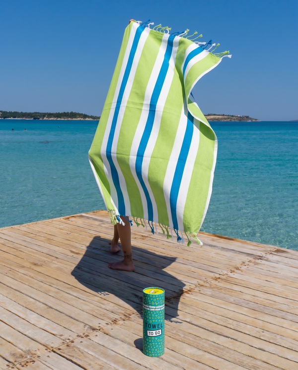 Woman using a Towel to Go Quick Dry Cotton Towel in Lime and Ocean Blue from the Coral Coast on the beach.
