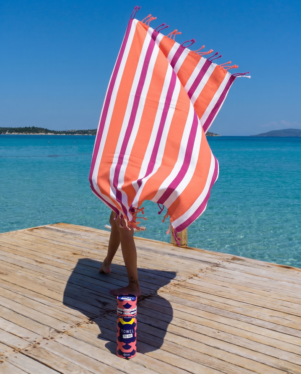 Woman using a Towel to Go Quick Dry Cotton Towel in Orange and Fuchsia from the Coral Coast on the beach.