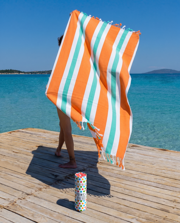 Woman using a Towel to Go Quick Dry Cotton Towel in Orange and Mint from the Coral Coast on the beach.