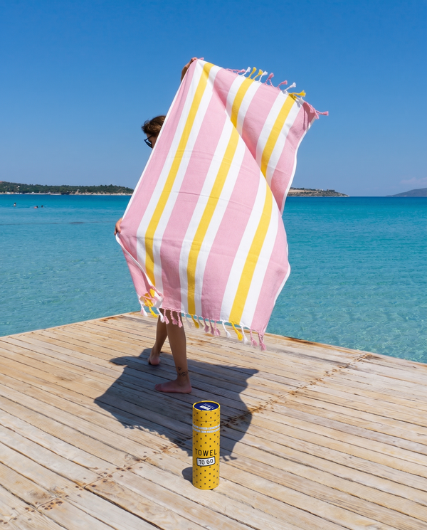 Woman using a Towel to Go Quick Dry Cotton Towel in Rose and Sunset from the Coral Coast on the beach.