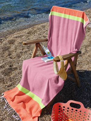 Dusty Rose & Orange 2-in-1 Beach Towel Bag draped over a wooden chair on a pebble beach