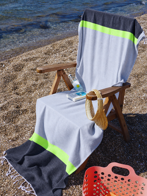 Grey & Charcoal 2-in-1 Beach Towel Bag draped over a wooden chair on a pebble beach