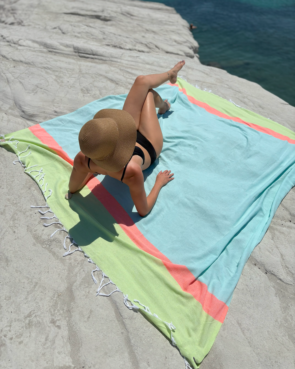 Person lying on a colorful beach towel by the water