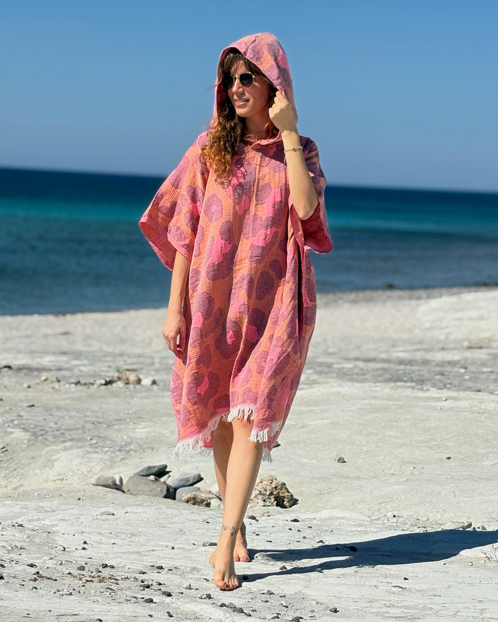 Woman using a Towel to Go Hooded Cotton Beach Poncho in Camel and Rose from the Neon Safari on the beach.