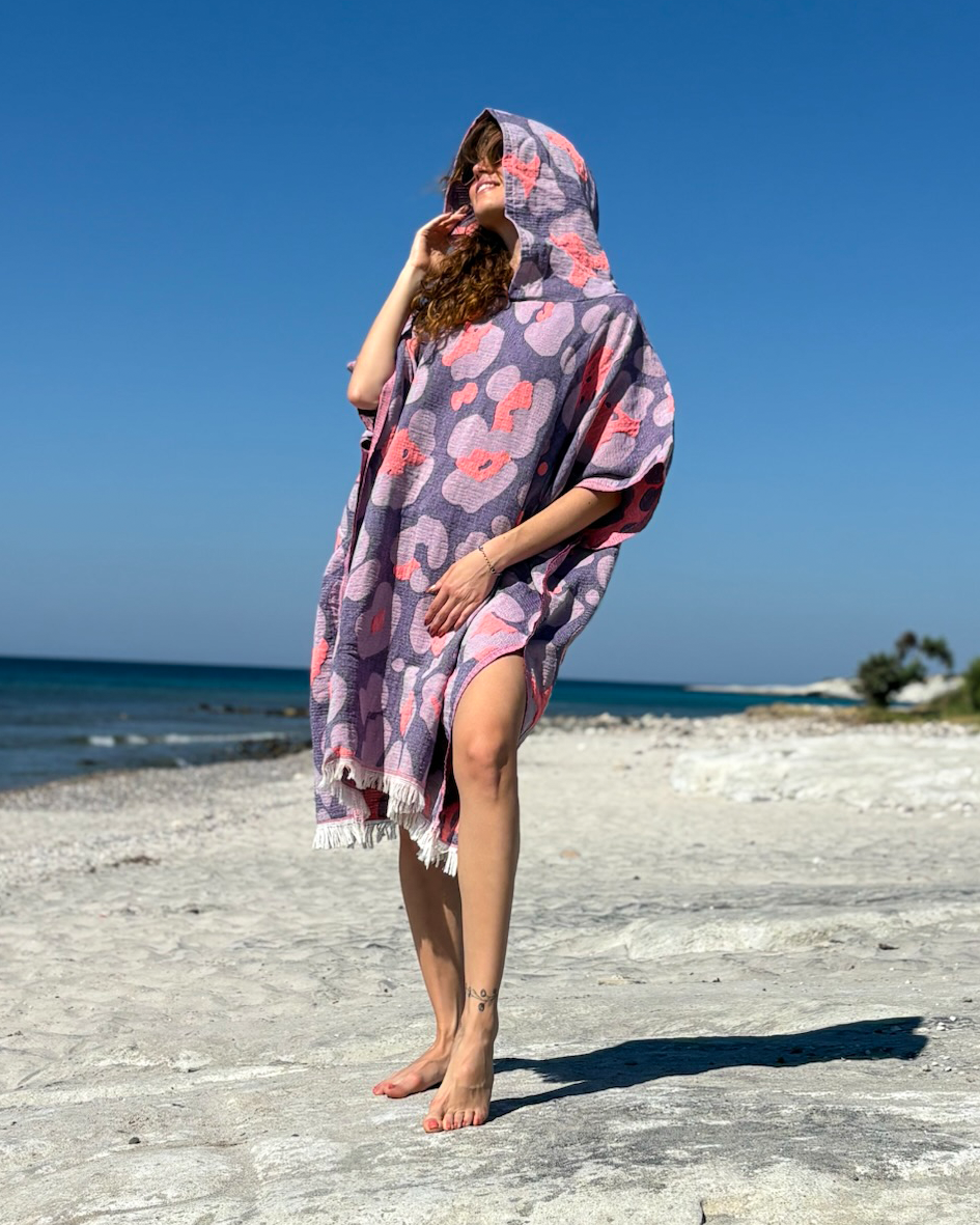Woman using a Towel to Go Hooded Cotton Beach Poncho in Lavender and Coral from the Neon Safari on the beach.