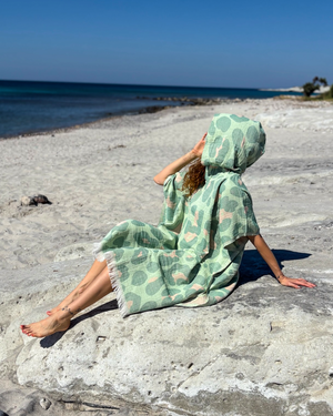 Woman using a Towel to Go Hooded Cotton Beach Poncho in Sage and Blush from the Neon Safari on the beach 2.