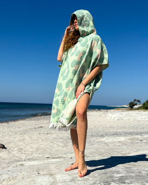 Woman using a Towel to Go Hooded Cotton Beach Poncho in Sage and Blush from the Neon Safari on the beach.