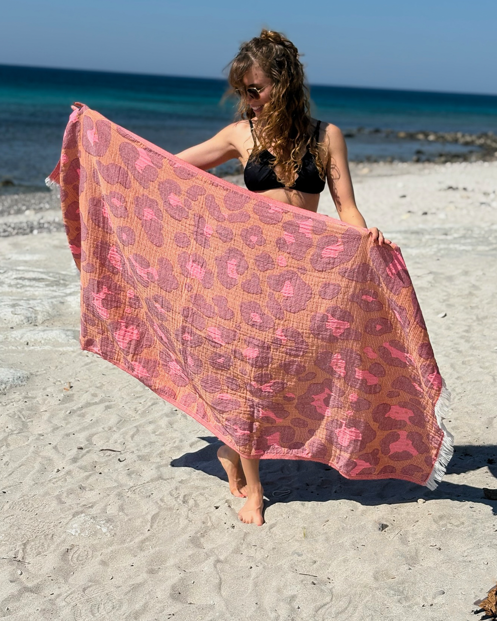 Woman using a Towel to Go Quick Dry Cotton Towel in Camel and Rose from the Neon Safari on the beach.