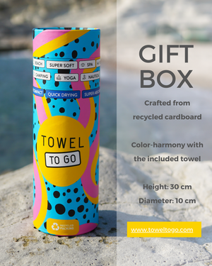 Colorful cylindrical gift box labeled 'Towel To Go' on a stone surface with text about its material and dimensions.